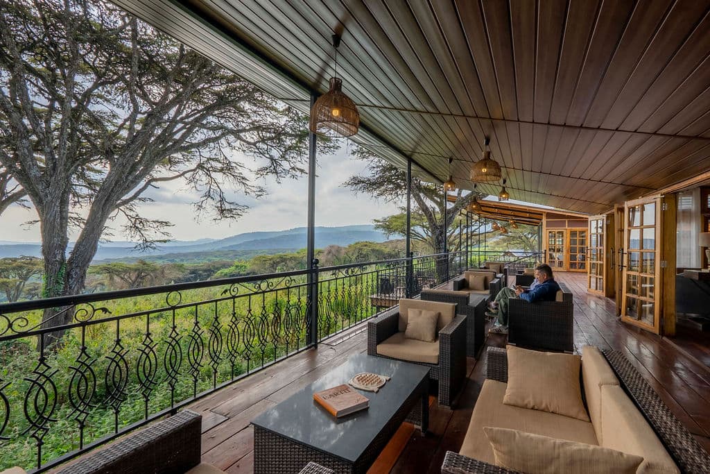 A guest reading on a timber lounge deck that looks out over acacia canopy to distant hills