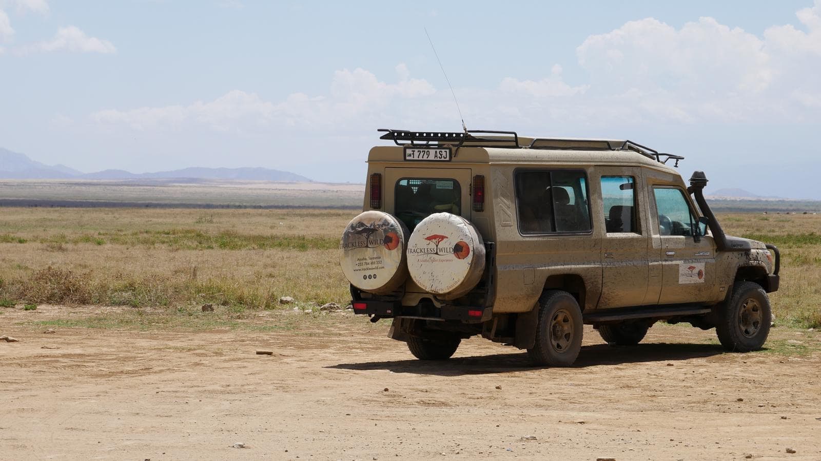 The safari vehicle small against a wide, dry plain